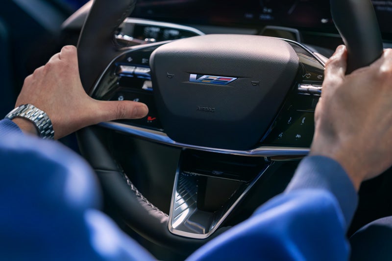 Close-up of a Man About to Press the V-Button on the 2026 OPTIQ-V Steering Wheel | Harvey Cadillac in Grand Rapids MI